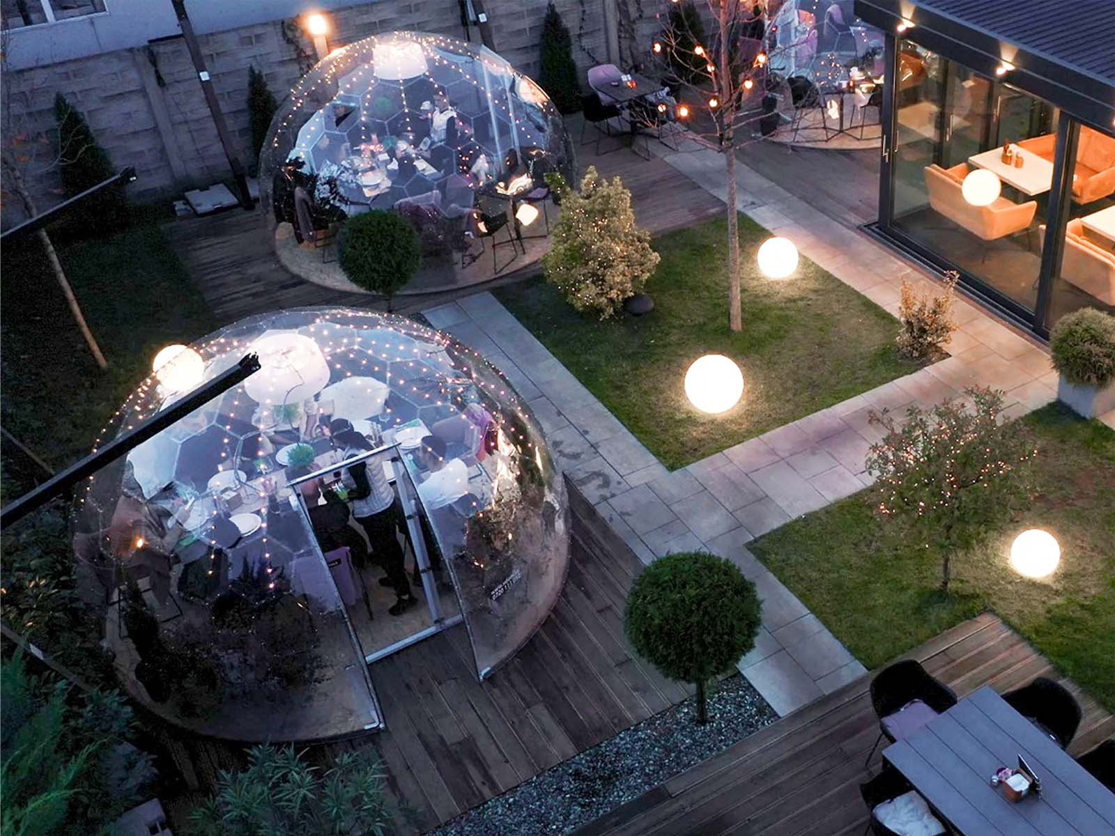 Bolle ristorazione trasparenti illuminate di sera in un giardino, viste dall’alto